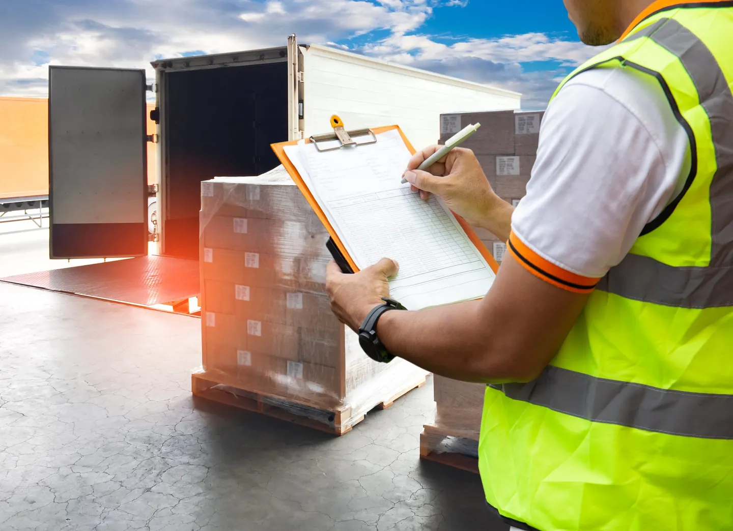 Agent in a high-visibility vest checking a load of parcels on a loading dock, shipping label in hand
